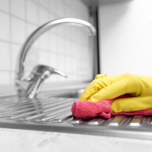 Hands in yellow gloves washing the kitchen sink.